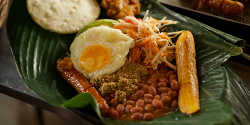 Try a typical bandeja paisa, made of red beans, sweet plantain slices, chorizo, white rice, ground meat, arepa paisa, avocado, fried egg, and fried pork belly.