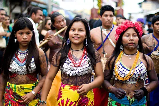 Photograph of three Indigenous women facing the camera as part of a parade in traditional clothing, Colombia megadiverse