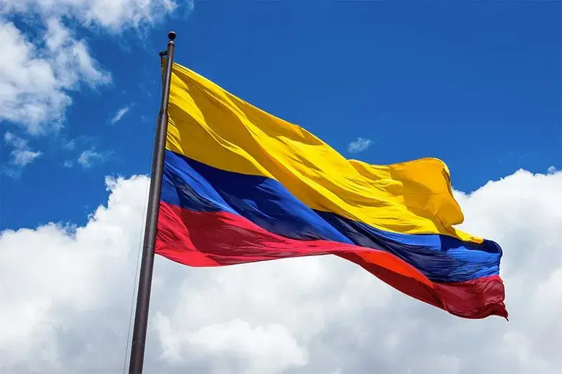 Colombian flag flying against a blue sky with clouds.