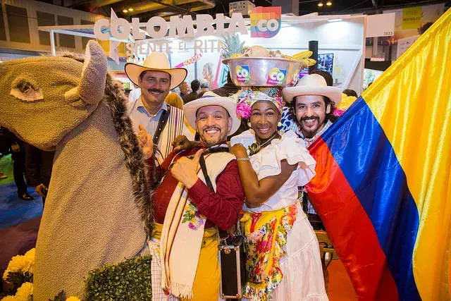Group of Colombians in traditional attire with flag at a fair.