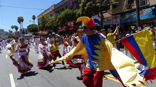 Colorful street parade with dancers and the Colombian flag.