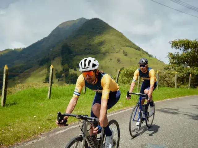 Dos ciclistas en carretera con paisaje montañoso colombiano.