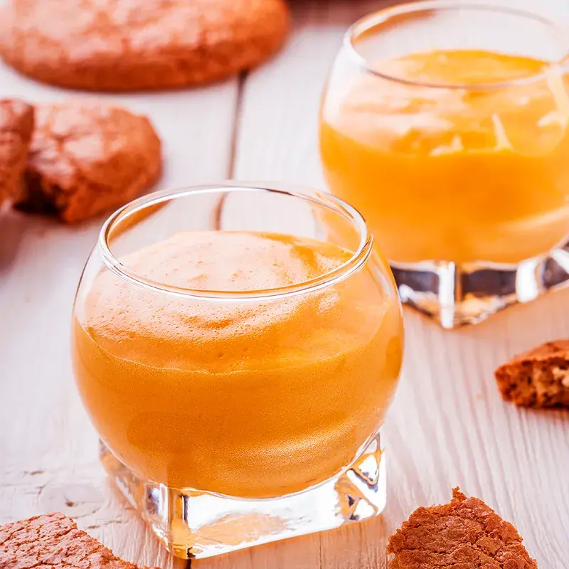 Dos vasos de sabajón cremoso acompañados de galletas sobre una mesa de madera.