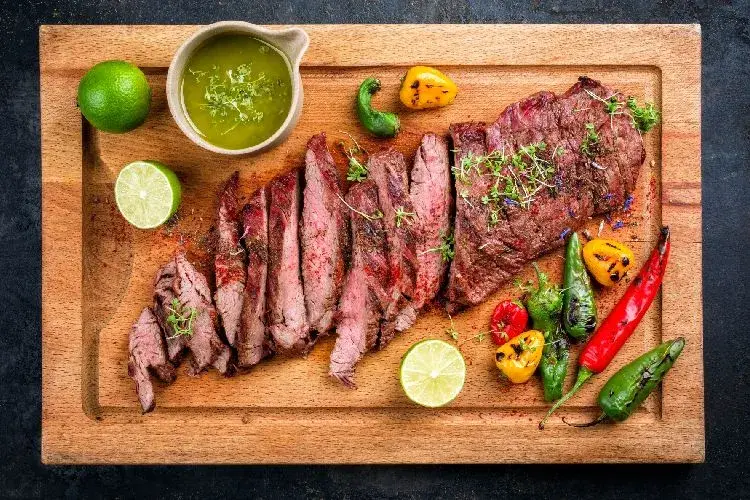 Plato de carne asada con ajíes, limón y salsa verde sobre tabla de madera