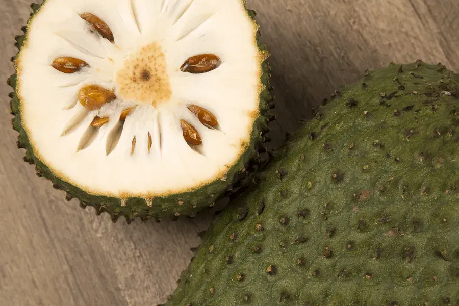 Soursop cut in half showing white pulp and brown seeds.
