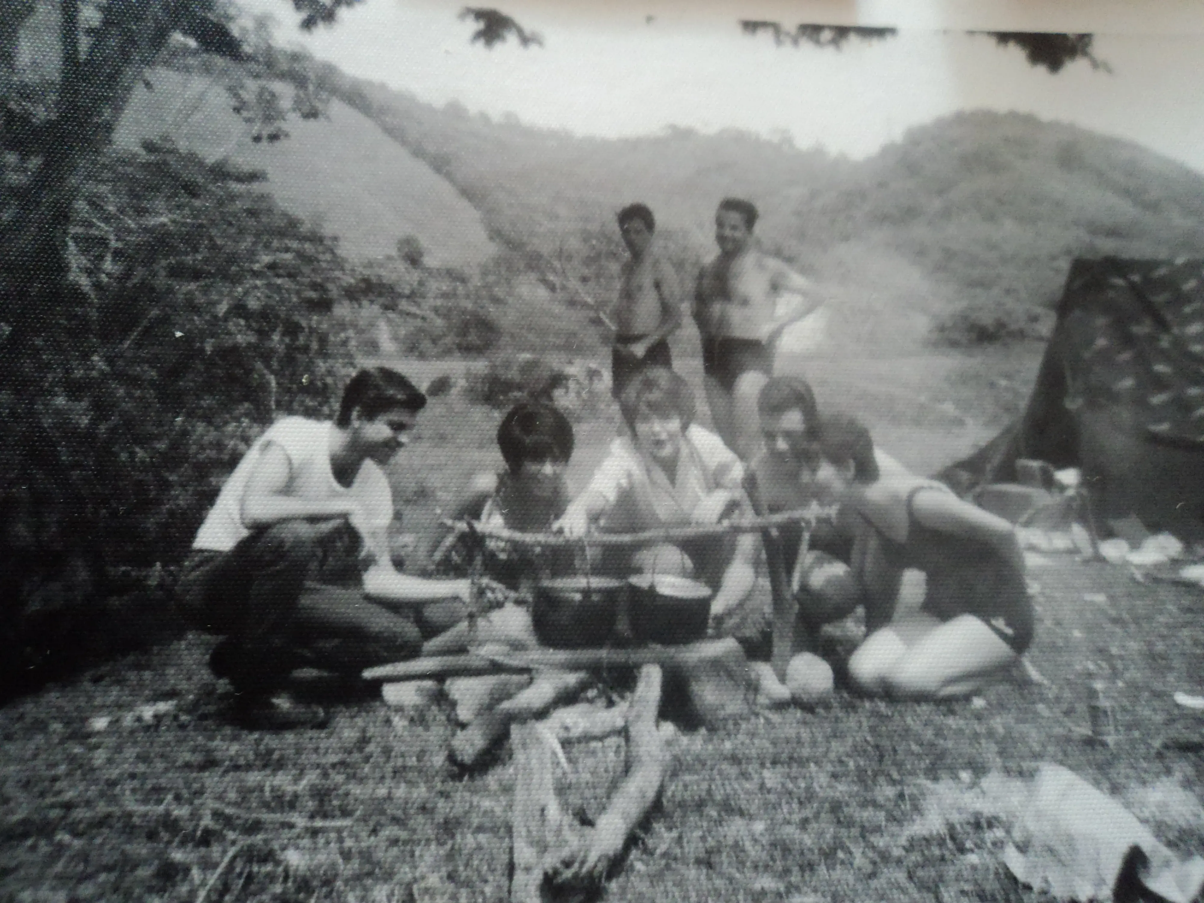 Group of young people cooking outdoors at a campsite surrounded by mountains and nature