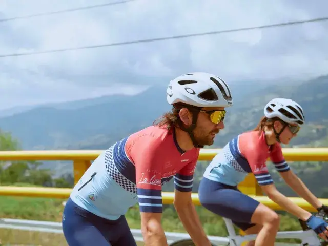 Dos ciclistas en carretera con paisaje montañoso al fondo.