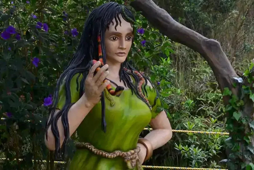 Sculpture of La Patasola holding a snake, surrounded by lush vegetation