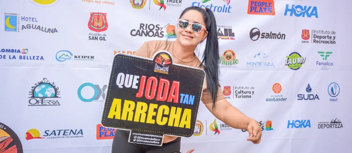 Woman with sunglasses holding a sign with a funny phrase at the Chicamocha Canyon Race sports event
