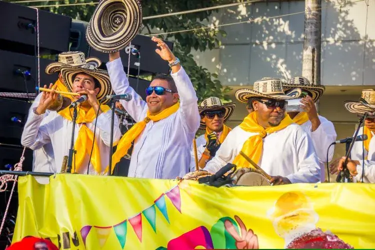 Grupo musical tocando cumbia colombiana en un festival, con músicos vistiendo camisas blancas, pañuelos amarillos y sombreros vueltiaos.