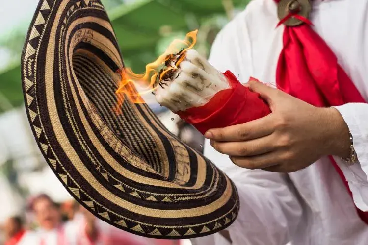 Primer plano de un sombrero vueltiao y una vela encendida envuelta en un pañuelo rojo.