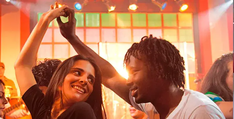 Couple dancing joyfully at a party with colorful lights and a festive atmosphere