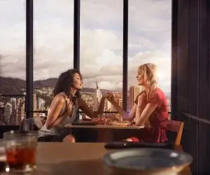 Couple of women sharing a meal in a restaurant overlooking the city at sunset.