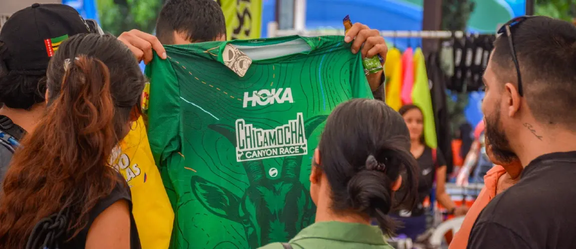 Person showing official green t-shirt of the Chicamocha Canyon Race in front of other attendees