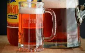 Jarra y vaso de refajo espumoso con botella de Colombiana en el fondo sobre una mesa.