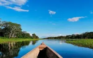 Canoa de madera navegando por río tranquilo bajo cielo azul con nubes.