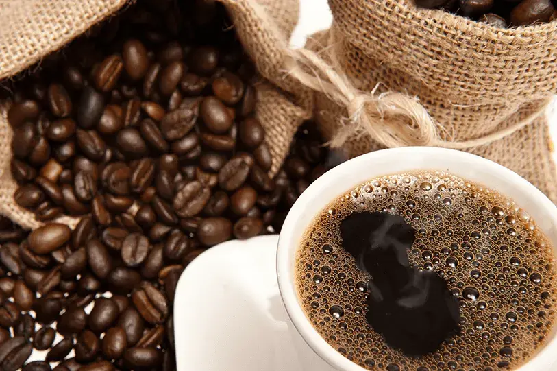 Taza de café negro junto a granos de café en sacos de yute.
