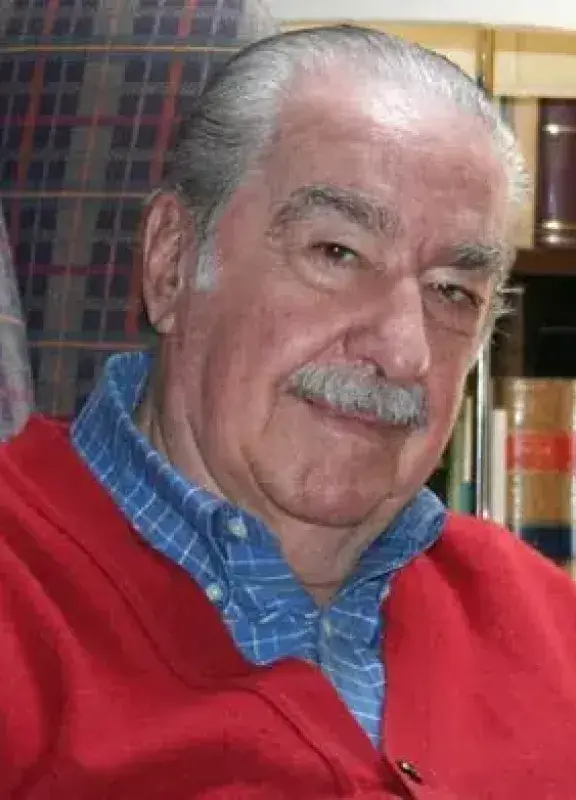 Hombre mayor con suéter rojo sentado Hombre mayor con suéter rojo sentado frente a estantería con libros