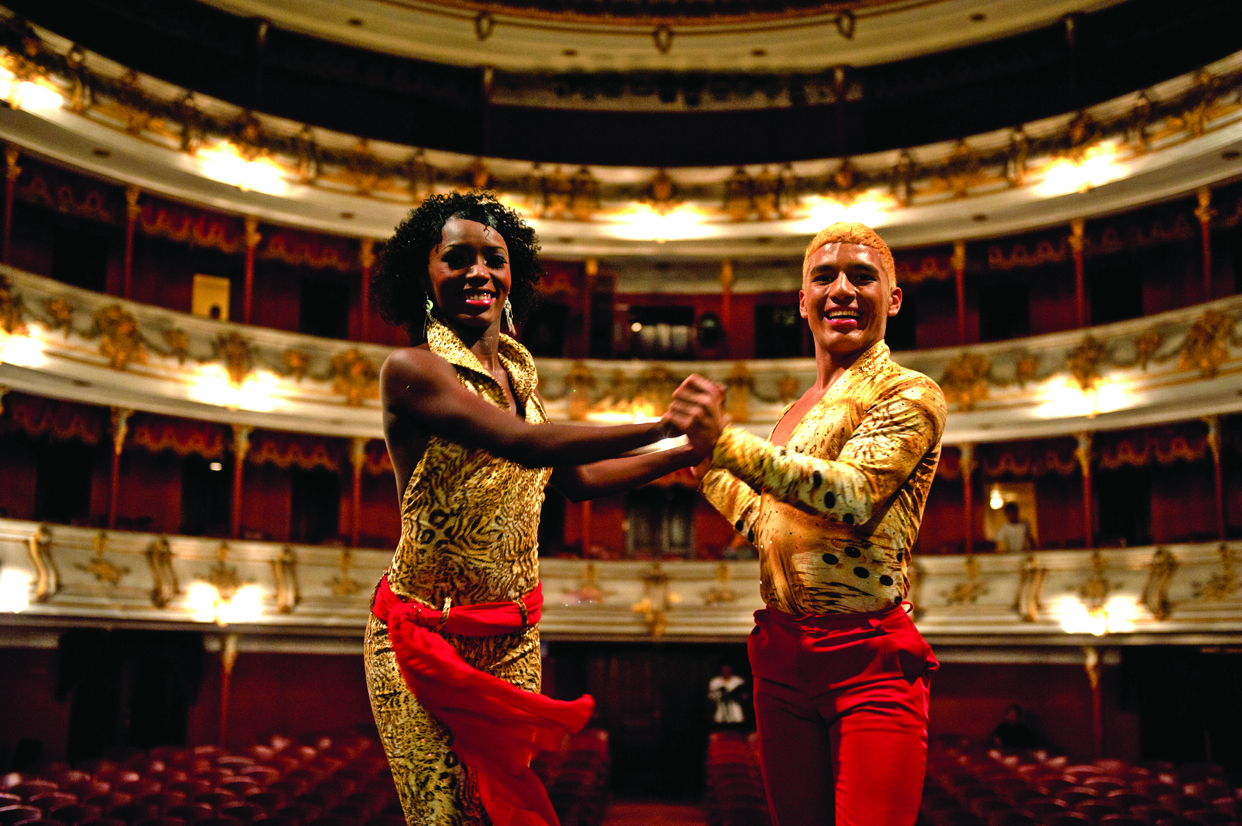 fotografia de dos bailarines de salsa viendo a la camara con fondo de un gran teatro, musica salsa, día de la raza 